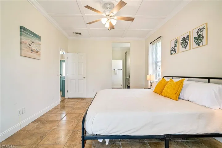 Bedroom featuring crown molding, a ceiling fan, light tile patterned floors, coffered ceiling, and connected bathroom