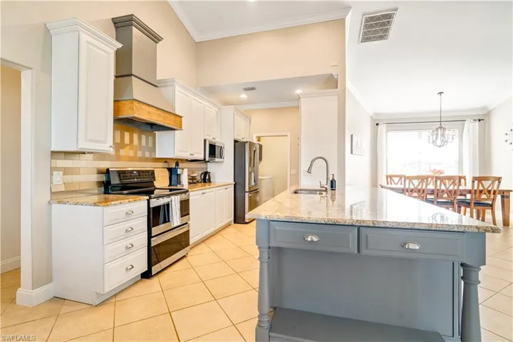 Kitchen with appliances with stainless steel finishes, backsplash, light stone counters, white cabinetry, and ornamental molding
