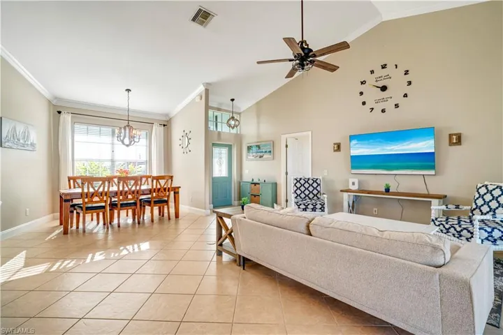 Living area with light tile patterned floors, ornamental molding, ceiling fan, high vaulted ceiling, and a chandelier