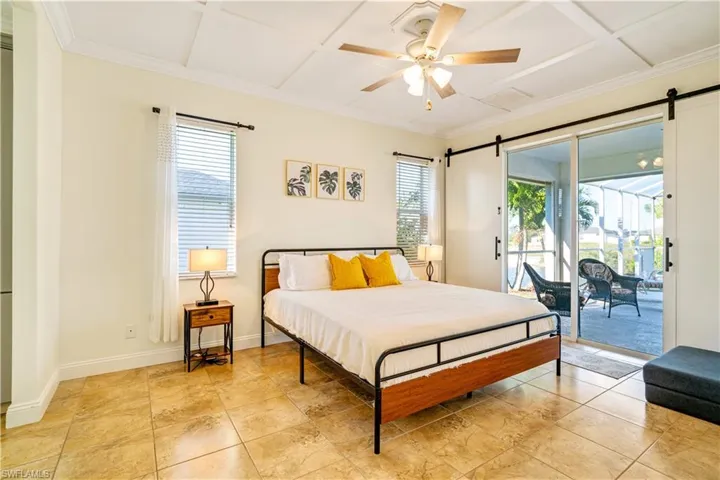 Bedroom with a ceiling fan, a barn door, access to exterior, light tile patterned floors, and coffered ceiling