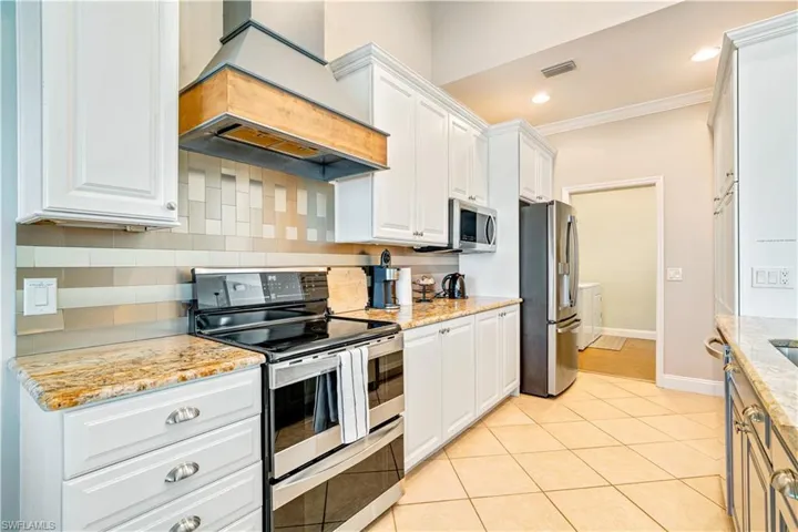 Kitchen featuring appliances with stainless steel finishes, backsplash, custom exhaust hood, white cabinets, and light stone countertops