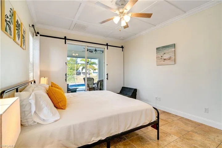 Bedroom with access to outside, a ceiling fan, a barn door, coffered ceiling, and crown molding