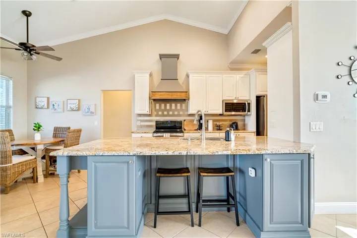Kitchen featuring crown molding, light tile patterned floors, light stone counters, a kitchen breakfast bar, and premium range hood