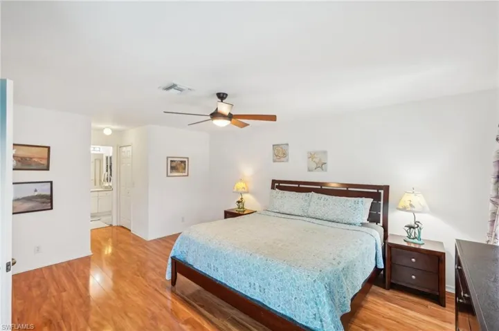 Bedroom with a ceiling fan, visible vents, light wood-type flooring, baseboards, and connected bathroom