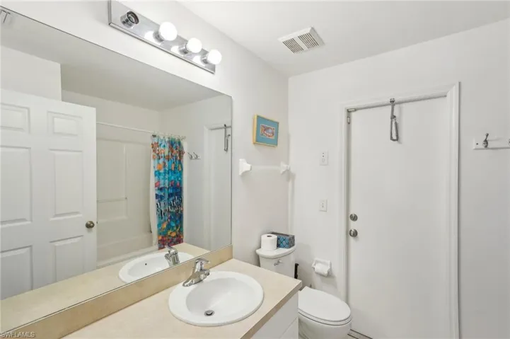 Full bath with vanity, toilet, curtained shower, and visible vents