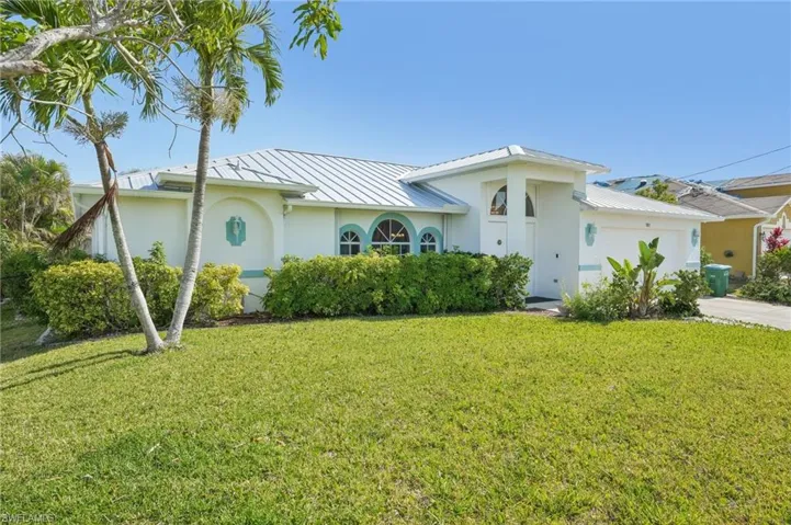 Single story home with a garage, stucco siding, a front yard, a standing seam roof, and metal roof