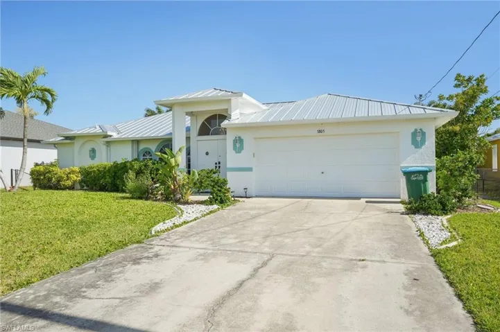 Ranch-style house featuring concrete driveway, a front lawn, stucco siding, metal roof, and an attached garage