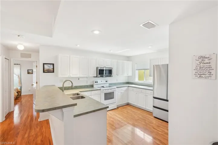 Kitchen with visible vents, a peninsula, white cabinetry, a sink, and stainless steel appliances