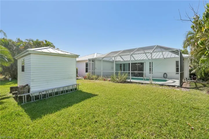 Back of property featuring a lawn, glass enclosure, and an outdoor pool