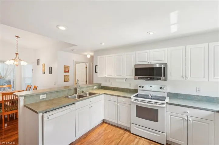 Kitchen featuring an inviting chandelier, a sink, white appliances, a peninsula, and light wood-type flooring