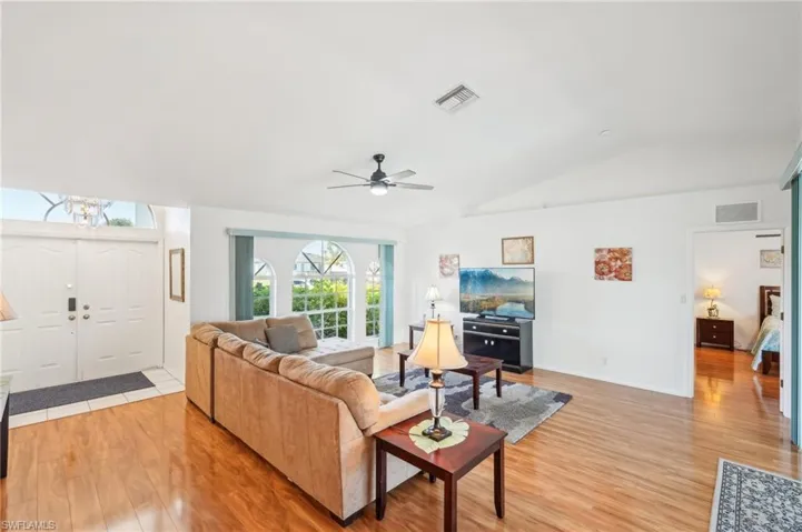 Living area with visible vents, light wood finished floors, lofted ceiling, and ceiling fan with notable chandelier