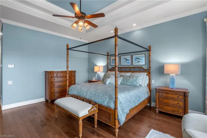 Bedroom featuring baseboards, ornamental molding, wood finished floors, and a raised ceiling