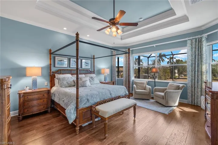 Bedroom with wood-type flooring, a raised ceiling, crown molding, and baseboards