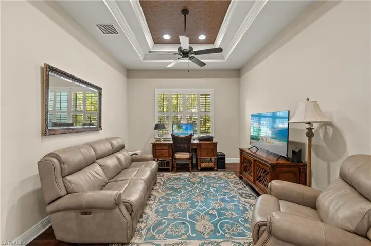 Office space with a tray ceiling, crown molding, baseboards, ceiling fan, and visible vents