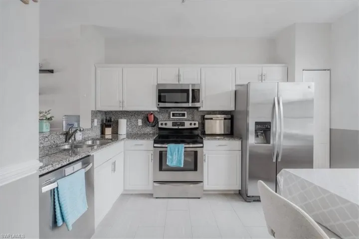 Kitchen featuring decorative backsplash, white cabinetry, appliances with stainless steel finishes, light stone countertops, and sink