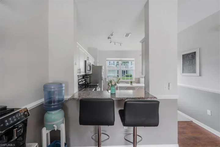 Kitchen featuring dark hardwood / wood-style floors, a kitchen breakfast bar, rail lighting, appliances with stainless steel finishes, and white cabinets