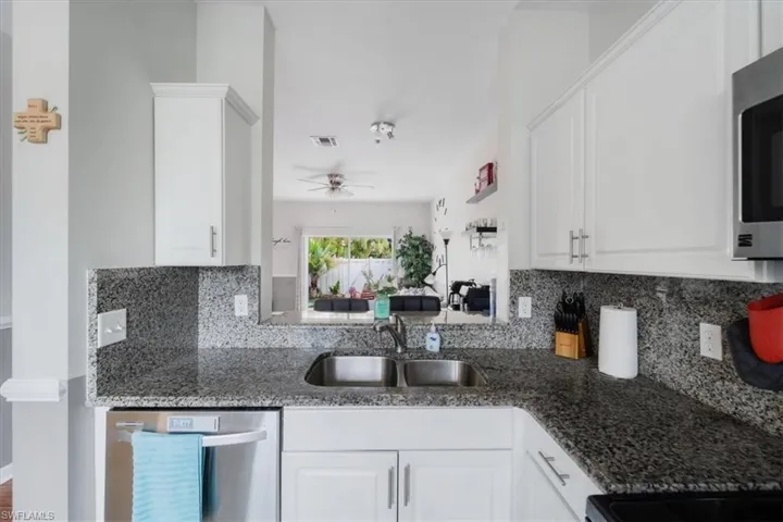 Kitchen with appliances with stainless steel finishes, dark stone countertops, white cabinetry, backsplash, and sink