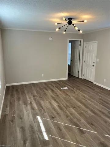 Spare room featuring a chandelier, dark wood-type flooring, a textured ceiling, and ornamental molding
