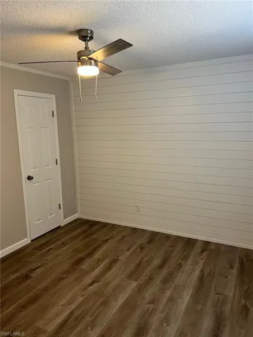 Unfurnished room featuring a textured ceiling, ceiling fan, wooden walls, crown molding, and dark hardwood / wood-style floors