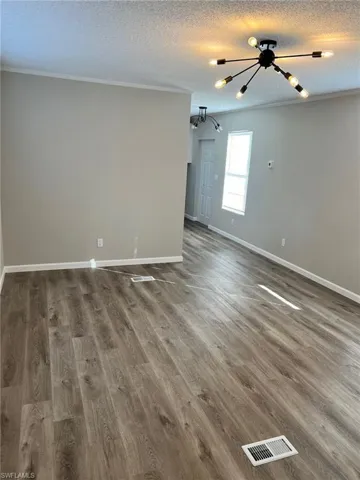 Empty room featuring a notable chandelier, wood-type flooring, a textured ceiling, and ornamental molding