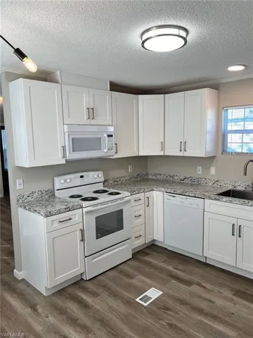 Kitchen with white cabinets, white appliances, dark wood-type flooring, and sink