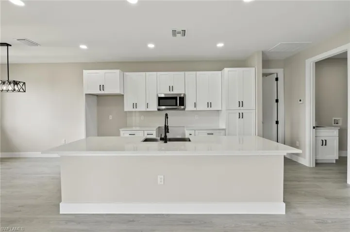 Kitchen featuring an island with sink, white cabinets, light hardwood / wood-style flooring, and hanging light fixtures