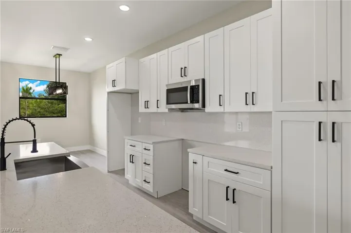 Kitchen with white cabinetry, sink, pendant lighting, and light stone counters