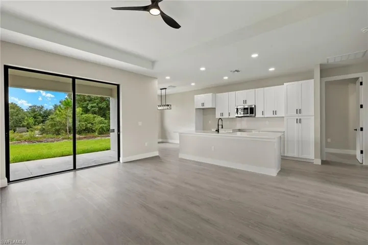 Kitchen featuring white cabinetry, pendant lighting, light wood-type flooring, ceiling fan, and a kitchen island with sink
