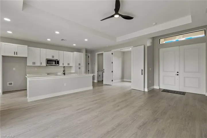 Kitchen with light wood-type flooring, a tray ceiling, an island with sink, white cabinets, and ceiling fan