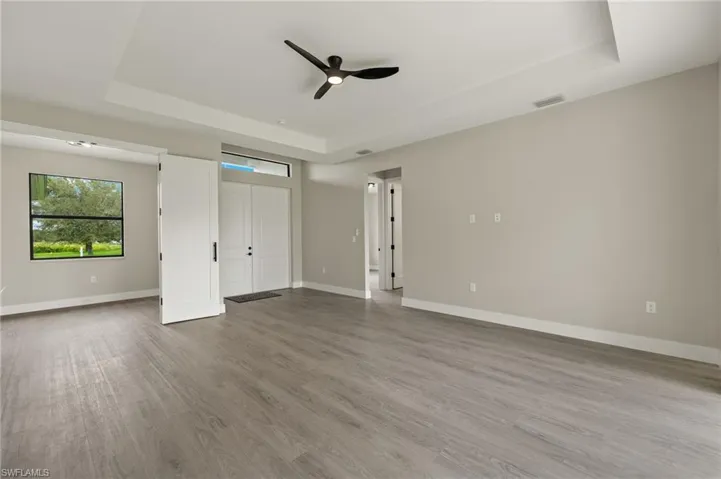 Unfurnished bedroom featuring ceiling fan, a raised ceiling, and light wood-type flooring