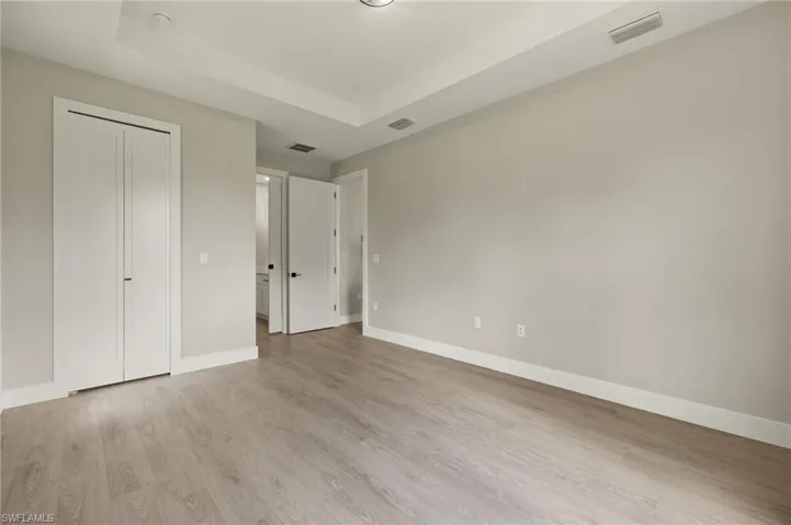 Unfurnished bedroom with light hardwood / wood-style floors, a tray ceiling, and a closet