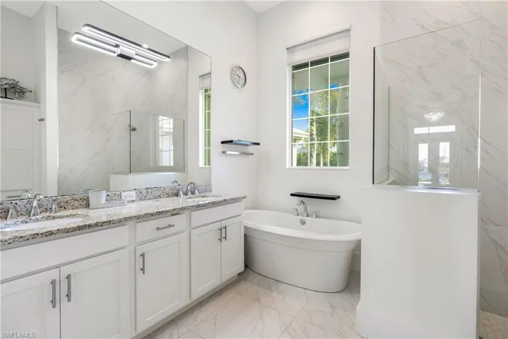 Full bath with a marble finish shower, double vanity, a freestanding bath, and light marble finish floors