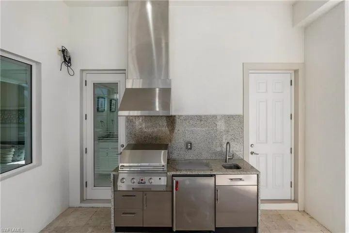Kitchen featuring backsplash, stainless steel fridge, wall chimney range hood, and light stone countertops