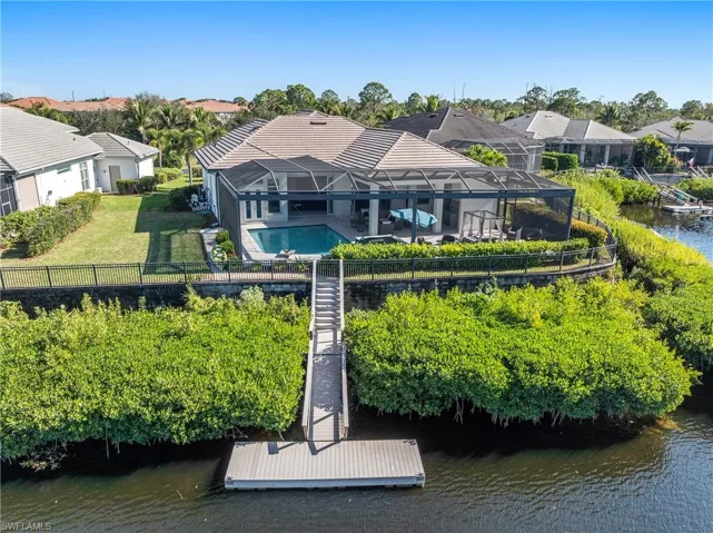 Back of property with a water view, a sunroom, a residential view, a fenced backyard, and a lanai