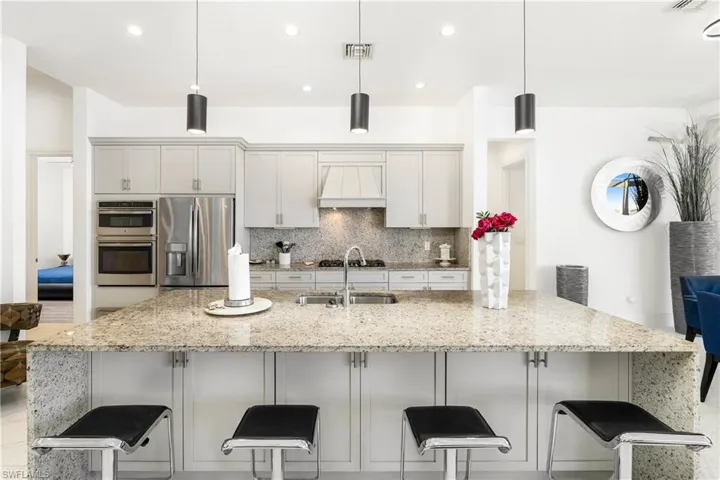 Kitchen with light stone counters, a large island with sink, pendant lighting, appliances with stainless steel finishes, and decorative backsplash