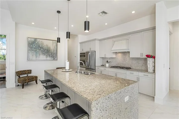 Kitchen featuring light stone countertops, decorative light fixtures, a breakfast bar area, custom range hood, and light marble finish floors
