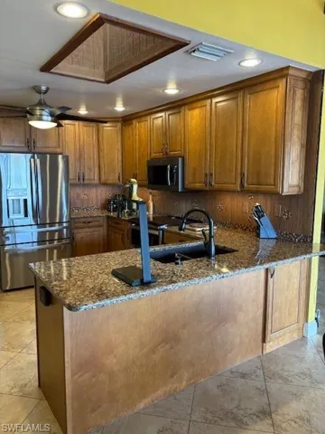 Kitchen featuring brown cabinetry, a peninsula, dark stone countertops, and fridge