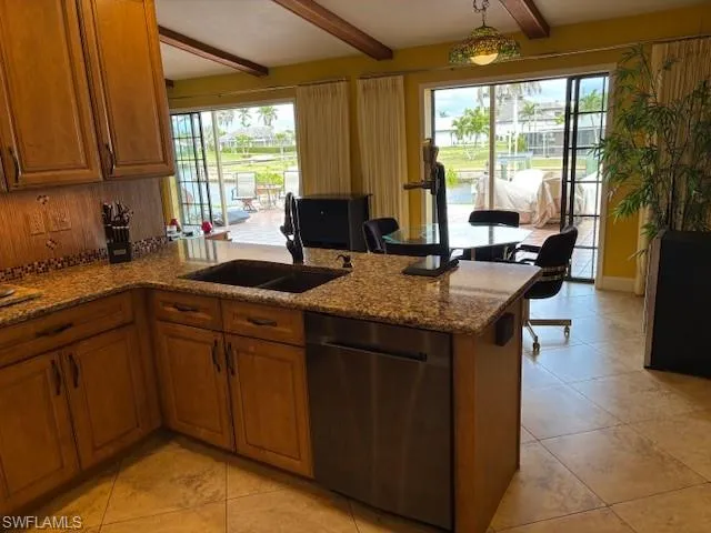 Kitchen featuring a peninsula, a sink, beam ceiling, brown cabinets, and dishwasher