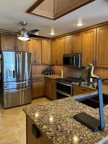 Kitchen featuring brown cabinetry, dark stone counters, a sink, and fridge