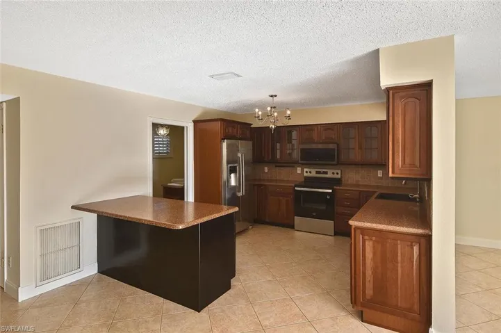 Kitchen with appliances with stainless steel finishes, a peninsula, a chandelier, decorative light fixtures, and light tile patterned floors