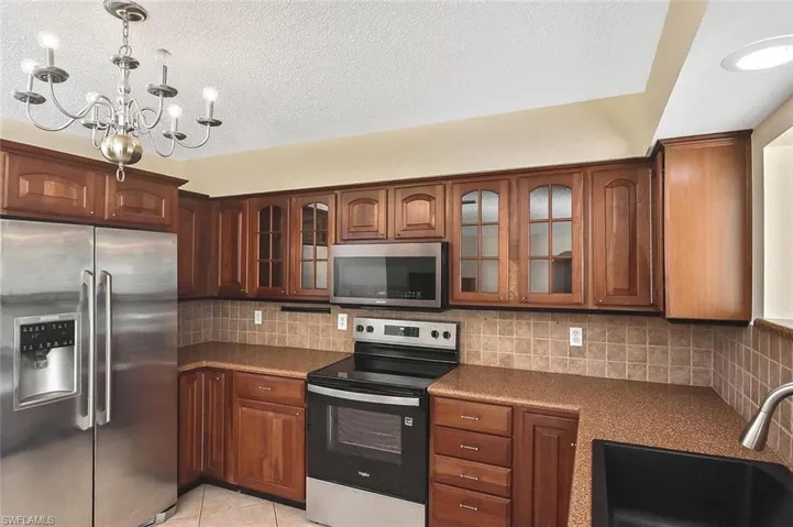 Kitchen with appliances with stainless steel finishes, glass insert cabinets, decorative backsplash, pendant lighting, and light tile patterned flooring
