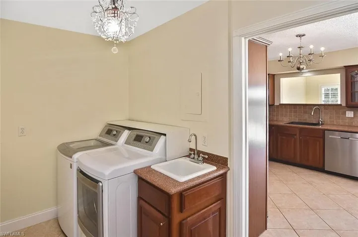 Laundry room with a chandelier, light tile patterned floors, washer and dryer, and electric panel