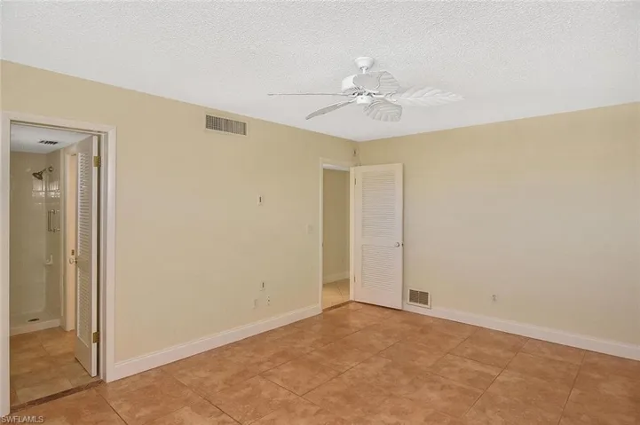 Unfurnished bedroom with a textured ceiling, a ceiling fan, ensuite bathroom, and light tile patterned floors