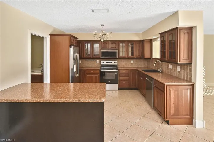 Kitchen with stainless steel appliances, glass insert cabinets, a chandelier, hanging light fixtures, and decorative backsplash