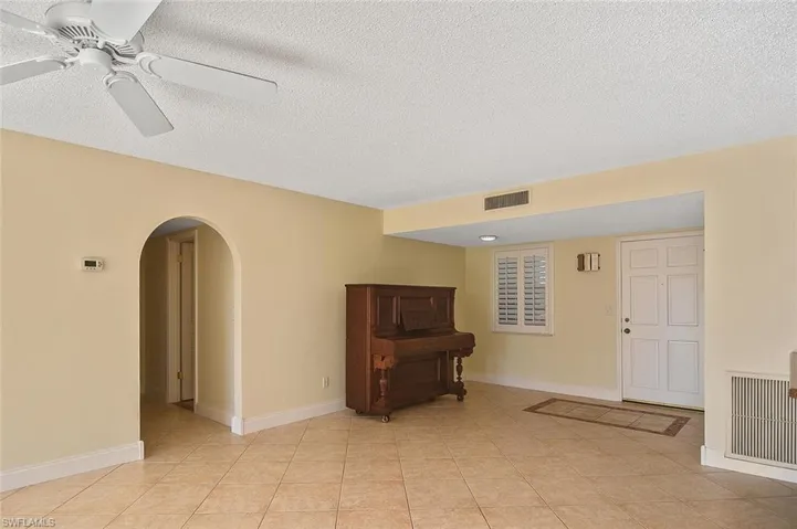 Unfurnished room featuring arched walkways, a textured ceiling, a ceiling fan, and light tile patterned floors