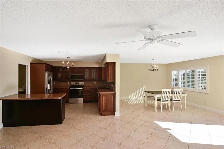 Kitchen with a chandelier, dark countertops, stainless steel appliances, light tile patterned floors, and glass insert cabinets