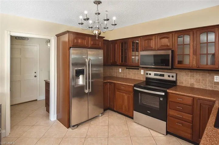 Kitchen featuring stainless steel appliances, glass insert cabinets, a chandelier, light tile patterned flooring, and hanging light fixtures
