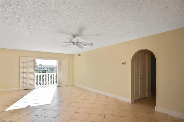Unfurnished room featuring arched walkways, a textured ceiling, a ceiling fan, and light tile patterned flooring