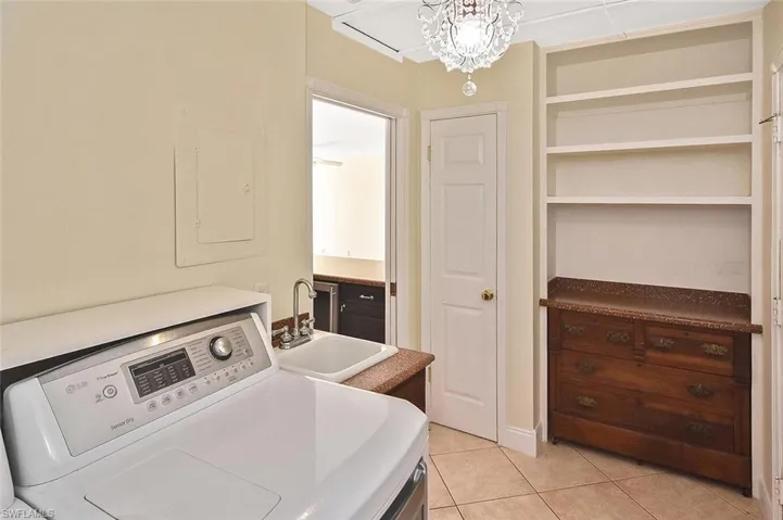 Washroom with washer / clothes dryer, light tile patterned floors, electric panel, and a chandelier