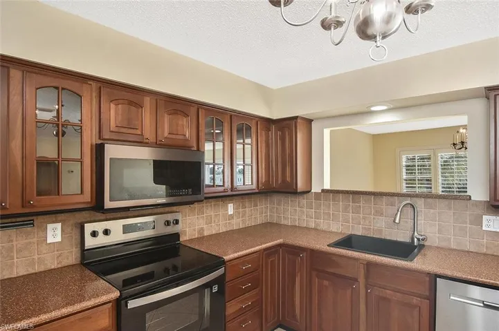 Kitchen featuring stainless steel appliances, glass insert cabinets, a chandelier, tasteful backsplash, and a textured ceiling